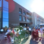 Skupina stanovalcev doma za starejše v invalidskih vozičkih in spremljevalcev z modrimi baloni pred vhodom doma v enoti Žabjak.