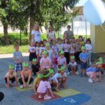 Skupina otrok v vrtcu izvaja nastop za stanovalce, oblečeni so v zelene naglavne trakove v obliki žabic.