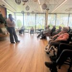 Oseba z mikrofonom pripoveduje zgodbo, poslušalci sedijo v polkrogu in zbrano poslušajo.