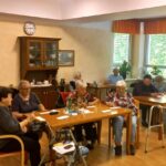 Stanovalci doma sedijo za mizami v skupnem prostoru in sodelujejo pri aktivnosti ob druženju.