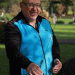 Oseba v modrem brezrokavniku drži kroglo in se nasmejano pripravlja na met v igri.