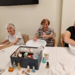 Skupina stanovalk se nasmejano prepusti negi rok ob mizici s kozmetičnimi pripomočki.