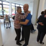 Stanovalka in stanovalec se z nasmehom zavrtita v plesu med dogodkom Mini Oktoberfest.