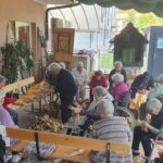 Skupina oseb v zavetju terase lička koruzo, ki je naložena v košarah pred njimi.