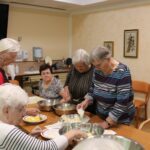 Stanovalke v kuhinji pripravljajo krompir in meso za paniranje.