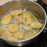 Kosi paniranega mesa se pražijo v vročem olju v loncu.