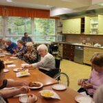 Stanovalci ob skupni mizi uživajo ob kosilu z ocvrtim krompirjem in mesom.