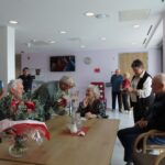 Osebe se zberejo okoli mize in čestitajo ob praznovanju visokega jubileja.