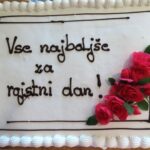 Bela torta z napisom »Vse najboljše za rojstni dan!« in okrasom iz rdečih vrtnic.
