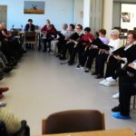 Skupina stanovalcev posluša pevski nastop ob praznovanju rojstnih dni v jedilnici doma.