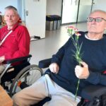 Dva stanovalca v vozičkih držita rože in se nasmihata ob praznovanju rojstnih dni.