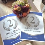 Na leseni mizi sta dve listi z napisom "2. mesto – met v tarčo" ter šopek pisanih suhih cvetov. Priznanji sta z modrim in sivim okvirjem.