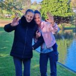 Stanovalka in zaposlena stojita ob ribniku, se nasmihata in mahata proti kameri.