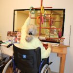 Stanovalka v vozičku izvaja gibalno vajo z barvnimi obroči na terapevtski konstrukciji.