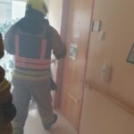 Gasilec v zaščitni obleki in s čelado se prebija po hodniku doma za starejše, kjer je zrak rahlo zadimljen. Vrata sobe so odprta, vaja simulira požarno situacijo.