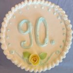 Slavljenska torta z napisom »90.«, okrašena s smetano in rumeno vrtnico.