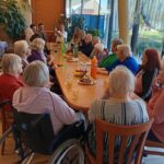 Stanovalci in obiskovalci sedijo ob praznični mizi ter nazdravljajo slavljencu.
