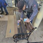 Stanovalec natančno barva leseno klop s čopičem.