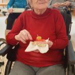 Stanovalka v rdečem puloverju uživa ob sendviču med skupnim srečanjem.