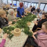 Skupina stanovalcev skupaj z osebjem ustvarja adventne venčke iz smrekovih vejic.