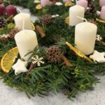 Adventni venčki z belimi svečami, začimbami in suhimi pomarančami, pripravljeni za praznično okrasitev.