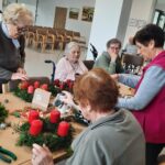 Stanovalke izdelujejo adventne venčke z rdečimi svečami in naravnimi materiali.