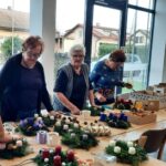 Skupina stanovalcev izdeluje adventne venčke z raznobarvnimi svečami in okraski.