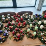 Razstavljeni adventni venčki z različnimi barvami sveč in naravnimi dekoracijami.