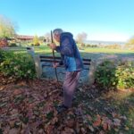 Stanovalec grabi listje ob klopi na sončen jesenski dan.