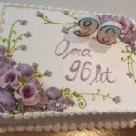 Bela rojstnodnevna torta z vijoličnimi okraski in številko 96 na svečkah.