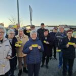 Skupina starejših oseb stoji na prostem in v rokah drži rumene vstopnice za koncert Domačih melodij.