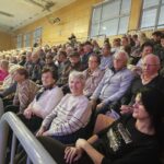 Velika skupina obiskovalcev, med njimi več stanovalcev doma, sedi na tribunih športne dvorane pred začetkom koncerta.