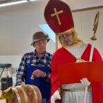 Moški v vlogi škofa in sodelujoči stanovalec skupaj izvajata simbolični krst vina.