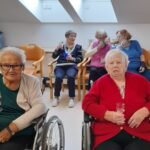 Stanovalke v invalidskih vozičkih in na stolih nazdravljajo ter se družijo ob dogodku.