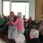 Dve stanovalke plešeta, medtem ko drugi spremljajo dogajanje.