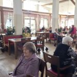 Stanovalci v jedilnici sedijo za mizami in čakajo na program.