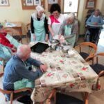 Stanovalci skupaj pripravljajo testo za pogačo ob kuhinjski mizi.