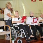 Stanovalka bere pesem ob pomoči zaposlenih na prireditvi »Ko si srečen«.