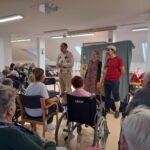 Stanovalci gledajo nastop igralske skupine v skupnem prostoru doma.