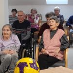 Skupina stanovalcev sedi v krogu in pozorno spremlja predstavo.