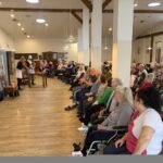 Stanovalci v dvorani gledajo komični prizor med dvema nastopajočima pred scensko kuliso.