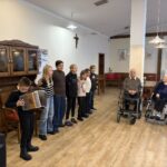 Skupina otrok z harmoniko nastopa pred stanovalci doma.