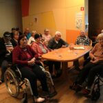 Skupina starejših oseb sedi v skupnem prostoru in posluša predstavitev o varnosti.