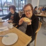 Starejša gospa nasmejano drži kos kruha, namazan z medom, med zajtrkom.