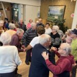 Stanovalci in zaposleni plešejo skupaj v jedilnici doma.