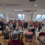 Otroci iz vrtca nastopajo pred stanovalci v skupnem prostoru doma.