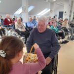 Deklica iz vrtca podarja darilo stanovalcu med druženjem.