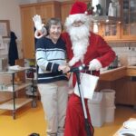 Stanovalka doma za starejše stoji ob Božičku, ki je oblečen v rdeč kostum in stoji na električnem skiroju v kuhinji.