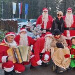 Skupinska fotografija obiskovalcev, oblečenih v Božičke, skupaj s stanovalci doma za starejše na prostem.