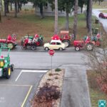 Božična povorka okrašenih traktorjev in starodobnega avtomobila na cesti pred domom, vozniki so oblečeni v Božičke.